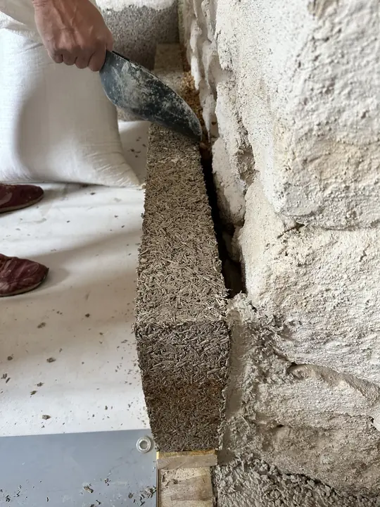 Maçon posant un bloc de chanvre contre un mur en pierre